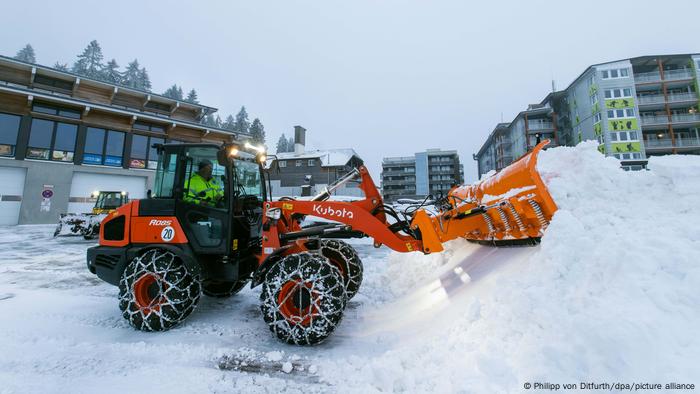 Ein Mitarbeiter eines Hotels befreit den Parkplatz mithilfe eines Baggers vom Schnee.