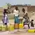 Frauen befüllen an einer Wasserpumpe Schüsseln und Plastikkanister  