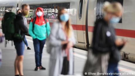 Reisende mit Corona-Schutzmasken auf einem Bahnsteig