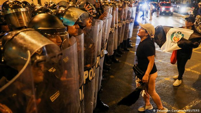 Eine Phalanx von schwer gerüsteten Polizisten steht einer leicht bekleideten Demonstrantin gegenüber 