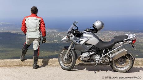 Ein Mann mit Motorrad genießt die Aussicht auf einem Berg bei Felantix auf Mallorca, Spanien.