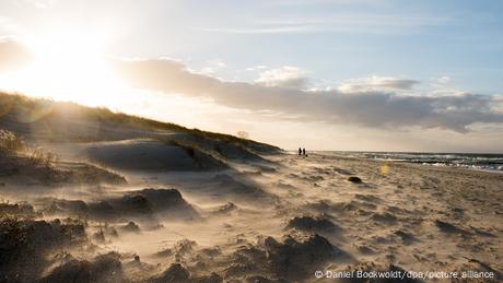 Spaziergänger sind bei Ahrenshoop bei starkem Wind am fast menschenleeren Strand an der Ostsee unterwegs.