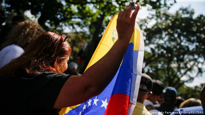 Mujer alza bandera venezolana con su mano derecha.