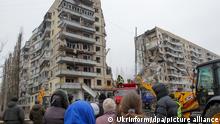 Menschen beobachten eine Such- und Rettungsaktion in dem Wohnblock, der von einer Rakete getroffen wurde, die von russischen Besatzern während eines massiven Raketenangriffs auf die Ukraine am Samstag, den 14. Januar, in Dnipro in der Zentralukraine abgefeuert wurde. Nach dem verheerenden russischen Raketenangriff auf das Wohnhaus in Dnipro werden in der ukrainischen Stadt noch immer viele Bewohner vermisst. Zugleich stieg die Todeszahl weiter an. +++ dpa-Bildfunk +++
