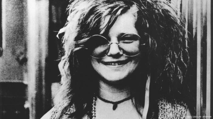 Janis Joplin lächelt mit wilder Mähne und großer Nickelbrille in die Kamera