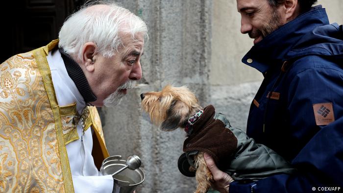 Ein Priester beugt sich zu einem Hund, beide küssen sich fast.