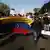 Dos personas portan una bandera de Venezuela. Detrás, una muchedumbre a pie.