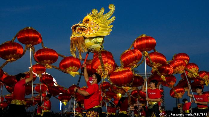 Personas ataviadas de rojo bailando y portando la máscara de la cabeza de un dragón.