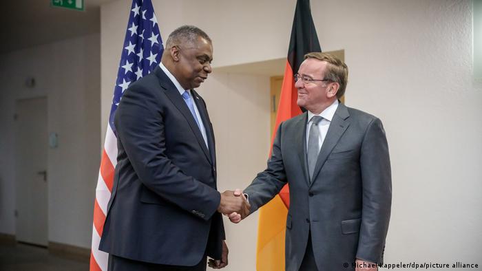 Deutschlands neuer Verteidigungsminister Boris Pistorius und sein US-Amtskollege Lloyd Austin geben sich die Hand im Hintergrund eine deutsche und US-amerikanische Flagge