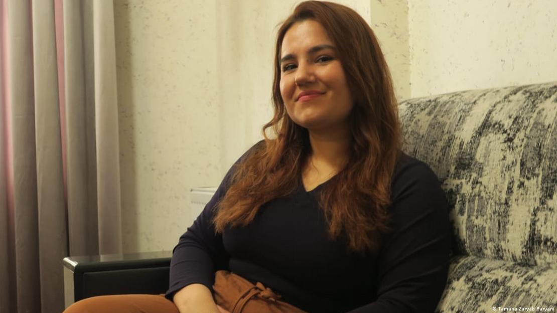 Zarmina Paryani sits on a sofa, smiling at the camera.