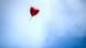 A heart shaped red balloon flies against a blue sky. A heart shaped red balloon flies against a blue sky.