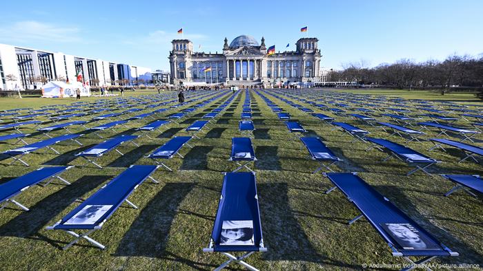 Camillas alineadas frente al edificio del Parlamento en Berlín con imágenes de afectados por el covid persistente.