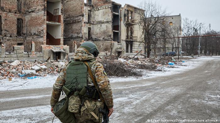 Ein Soldat geht an zerstörten Häusern vorbei. Die Straßen sind leicht vom Schnee bedeckt. 