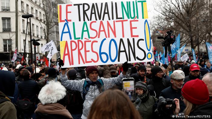 En medio de las manifestaciones del 19 de enero, en París, un hombre levanta una pancarta que dice trabajar es malo para la salud después de los 60 años.