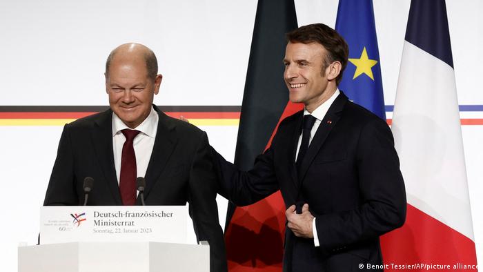 Scholz und Macron an einem Rednerpult mit National- und EU-Flaggen im Hintergrund beim Deutsch-französischen Ministerrat