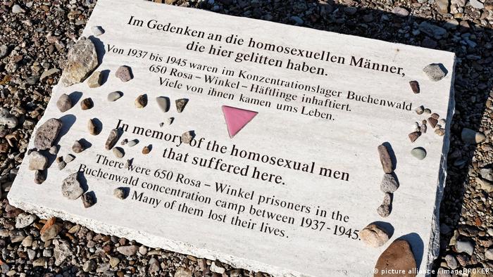 Eine hellgraue Steinplatte in der KZ-Gedenkstätte Buchenwald liegt auf dem Boden. In deutscher und englischer Sprache wird an die rund 650 inhaftierten und teilweise ermordeten homosexuellen Häftlinge erinnert. In der Mitte ein rosa Winkel in Form eines Dreiecks, mit dem die Nazis schwule Männer stigmatisierten. 