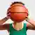 Stock image of a female basketball player holding a basketball in front of her face