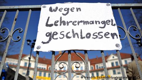Auf einem Gitter vor einem Gebäude hängt ein Schild: „Wegen Lehremangel geschlossen“ (Quelle: Hendrik Schmidt/dpa/picture alliance)