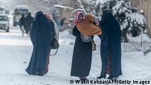 Frauen in Burkas tragen Kinder auf verschneiter Straße in Kabul