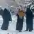 Frauen in Burkas tragen Kinder auf verschneiter Straße in Kabul