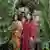 Drei Frauen und ein Mann in Indigenen-Kostümen stehen im Urwald