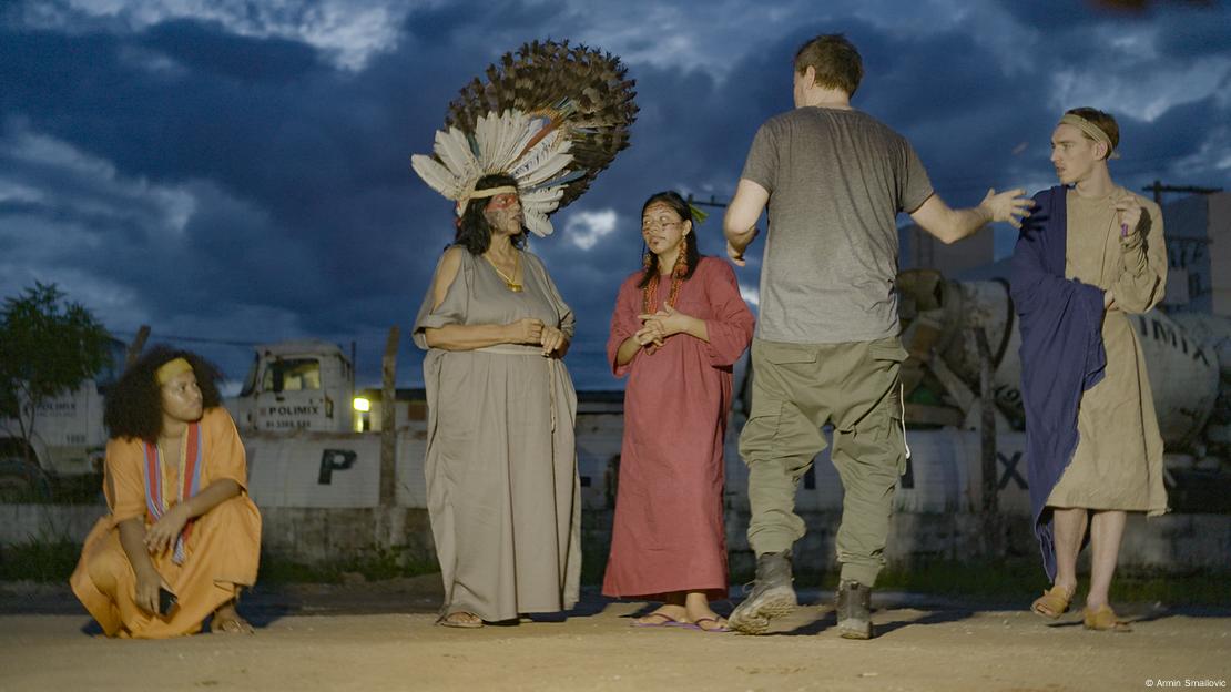 Scene Antigone in the Amazon, several men and wopmen on stage, a man stands in front of them and seems to be explaining something.