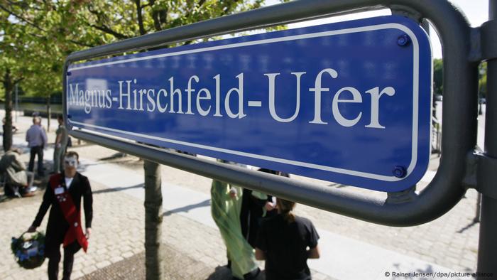 Magnus-Hirschfeld-Ufer steht in weißen Buchstaben vor einem blauem Hintergrund auf einem Schild an einer Promenade der Spree in Berlin 