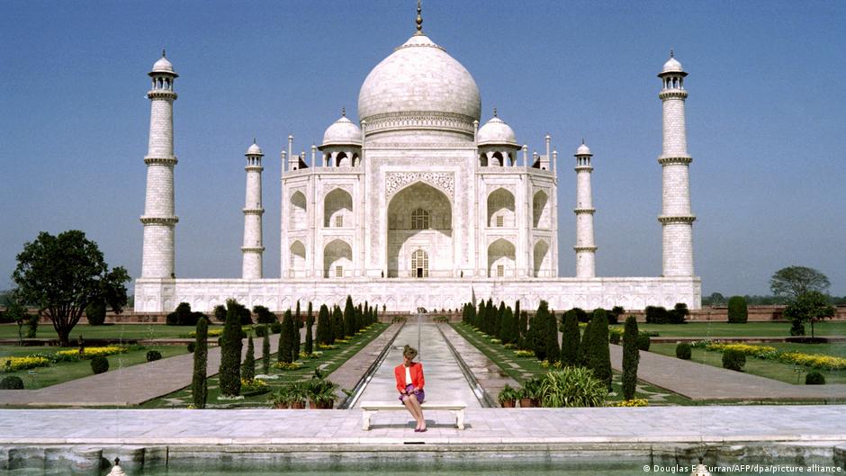 Diana sitzt ganz alleine auf einer Bank vor dem Taj Mahal, einem gigantischen Grabmal aus weißem Marmor.