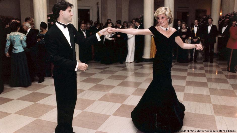 Diana im dunkelblauen Samtkleid und John Travolta im Smoking tanzen miteinander, umringt von weiteren Partygästen.