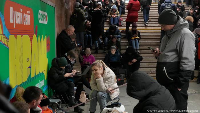 Varias personas esperan atentos a sus teléfonos celulares en las instalaciones del suburbano de la capital ucraniana durante una alarma aérea en una imagen de hoy.
