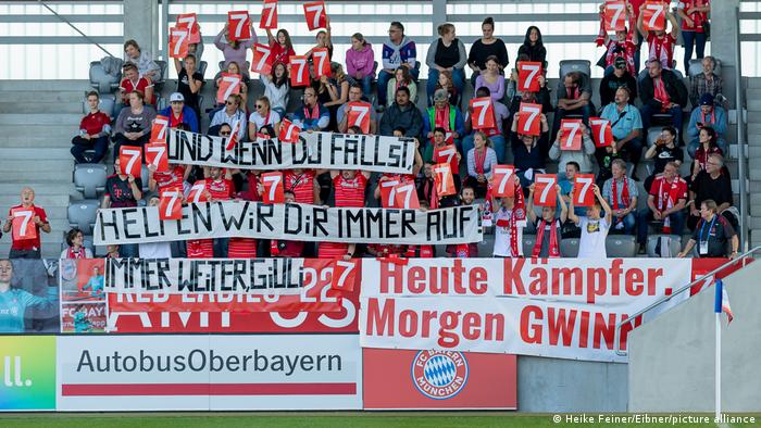 Bayern Fans halten Spruchbänder hoch mit Genesungswünschen für Giulia Gwinn nach deren zweitem Kreuzbandriss. 