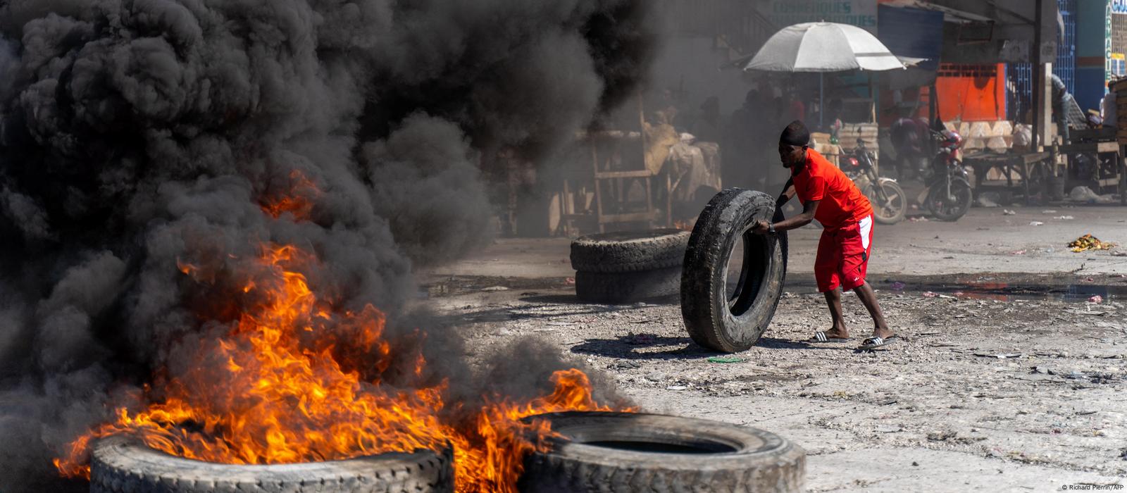 A man rolling a tire into a blockade of burning tires on the streets of Port-au-Prince