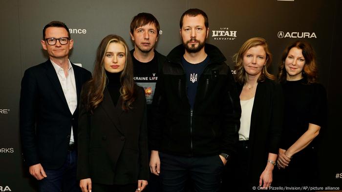 Mstyslav Tschernow, Evgeniy Maloletka und Vasilisa Stepanenko stehen mit weiteren Mitarbeitenden vor einer schwarzen Wand des Sundance-Festivals und posieren für die Kamera