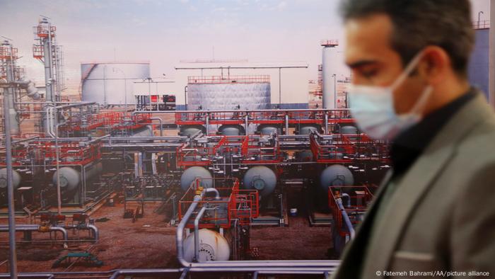 Hombre con mascarilla ante una refinería de petróleo.