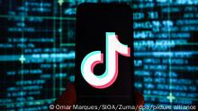 Das Logo der Video-App TikTok ist auf einem Smartphone vor einem Bildschirm mit Börsenkursen im Hintergrund zu sehen. Die EU-Kommission hat dem Chef der beliebten Video-App Tiktok, Shou Zi Chew, weitreichende Sanktionen angedroht, sollte sich sein Unternehmen in Zukunft nicht an europäische Regeln halten. (zu dpa Lebensbedrohliche Inhalte: EU-Kommission droht Tiktok mit Verbot) +++ dpa-Bildfunk +++