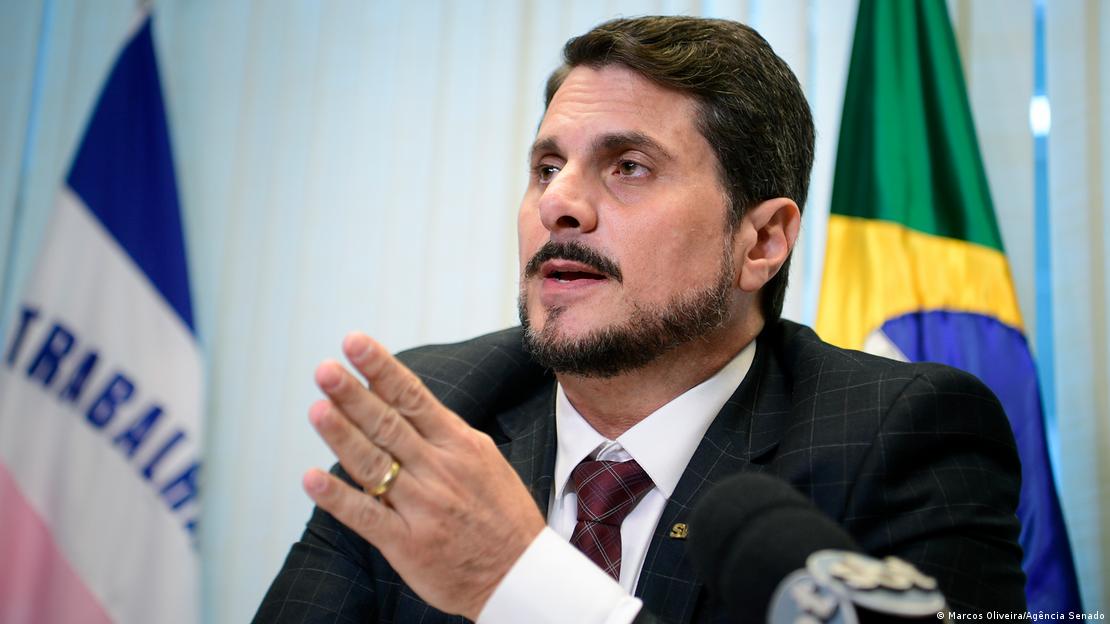 Marcos do Val, sentado, em frente a uma bandeira do Brasil