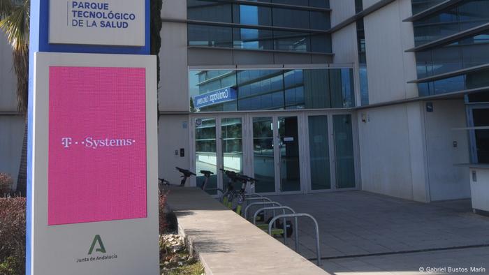 El logo de T-Systems, filial de servicios digitales de Deutsche Telekom, en una pantalla a la entrada del edificio, donde también se ve el logo de la Junta de Andalucía (gobierno regional) y se lee Parque Tecnológico de la Salud.