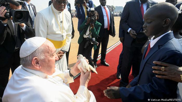 Südsudan, Besuch von Papst Franziskus: Der Papst hält bei der Ankunft eine Taube in der Hand, ein Kind begrüßt ihn