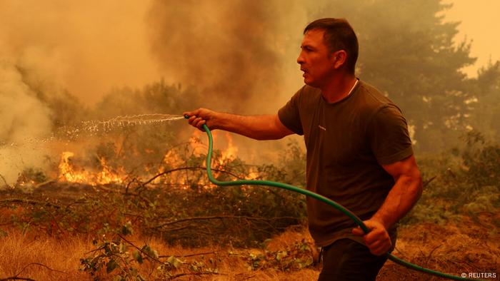 Un hombre con una manguera tira un poco de agua a las llamas.