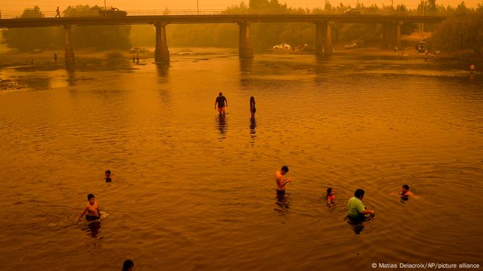 Personas vadean en el río bajo un cielo enrarecido por el denso humo de los incendios forestales, en Renaico.