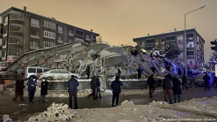 Menschen stehen um ein eingestürztes Gebäude in einer verschneiten Stadt