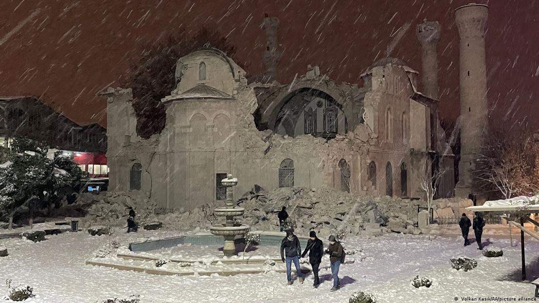 Pessoas caminham em meio à neve em frente à mesquita que ficou destruída depois de terremoto na Turquia