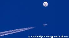Der weiße Spionageballon vor blauem Himmel. Darunter ein Kampfflugzeug, das einen Kondensstreifen nach sich zieht