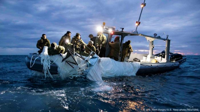 Hombres sobre una lancha recogen trozos de plástico blanco del mar.