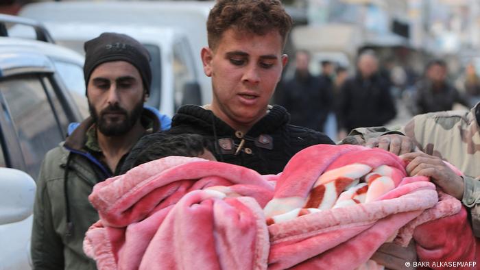 A young man holds the body of a child wrapped in a blanket