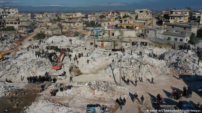 Eine Luftaufnahme zeigt Menschen die nach dem Erdbeben in der türkisch-syrischen Grenzregion unter Trümmern von Gebäuden nach Verschütteten suchen und dabei von Baggern unterstützt werden
