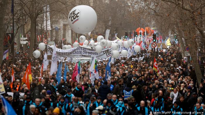 Menschen mit Transparenten, Bannern und weißen Luftballons laufen in einem Protestzug durch eine Straße in Paris.