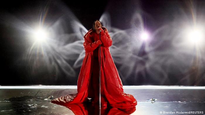 Rihanna in rotem, ausladendem Umhang auf der Bühne.