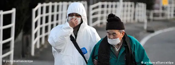 Ein Helfer im Schutzanzug begleitet einen älteren Mann im verstahlten Gebiet nahe dem AKW Fukushima (Foto: dpa)
