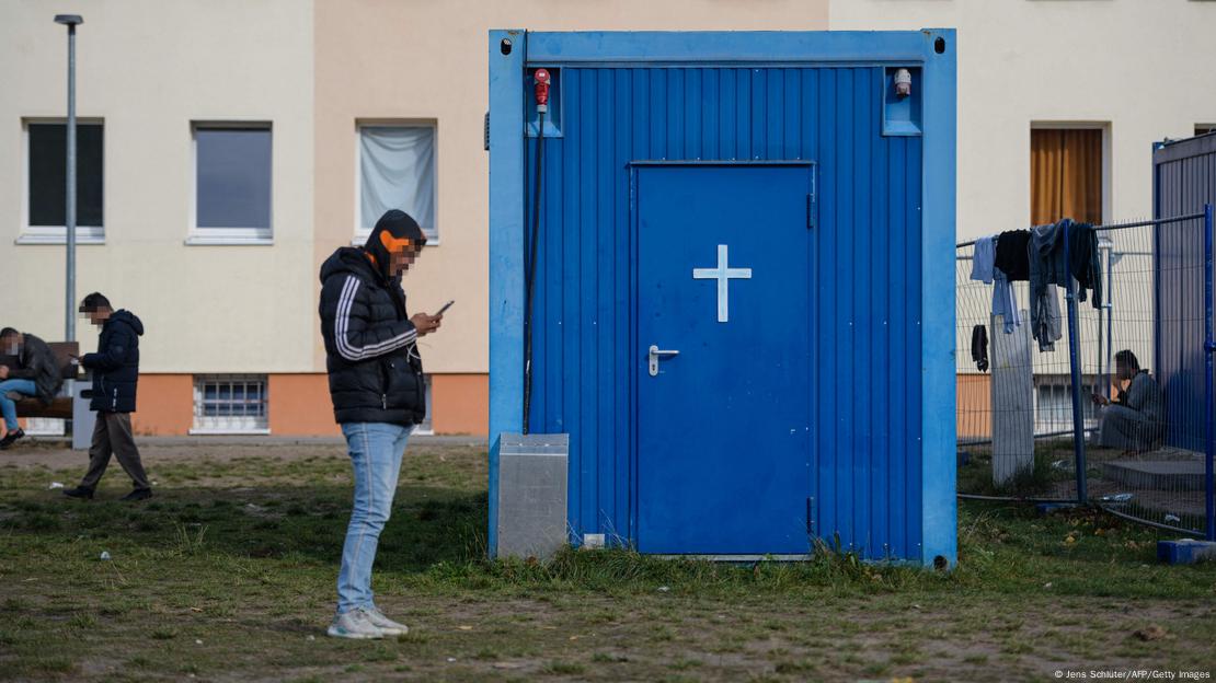 refugee checks his mobile phone standing nex to the entrance to a temporary prayer room